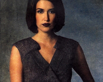 May include: A woman wearing a black sleeveless dress with a V-neckline. The dress has a textured fabric and a fitted silhouette.