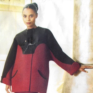 May include: A woman is wearing a red and black jacket with a red skirt and black tights. She is standing in front of a white wall.