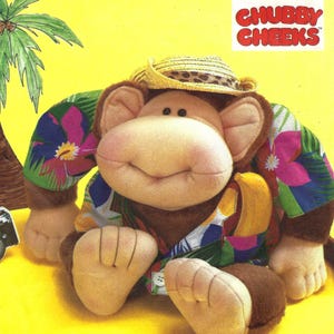 May include: A plush monkey wearing a straw hat and a colorful Hawaiian shirt. The monkey has a smiling face and is holding a banana. The image includes the text "CHUBBY CHEEKS" and "crafts/ouvrages".