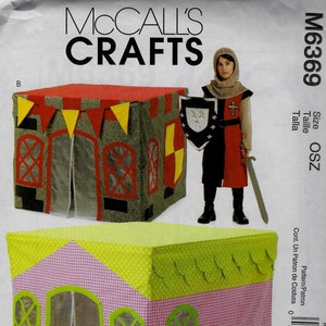 May include: A sewing pattern for a playhouse with two different designs. One design is a castle with a red roof and yellow and red accents. The other design is a cottage with a pink and green checkered pattern and green trim. The pattern is from McCall's Crafts and the pattern number is M6369.