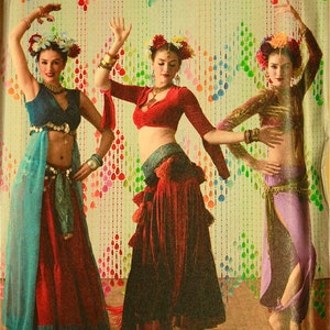 May include: Three women wearing colorful dance costumes with fringe and beaded accents. The women are posing in front of a colorful background with a curtain of beads. The image includes the text "Simplicity the dance studio".