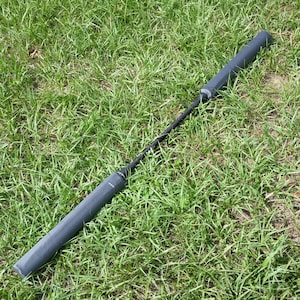 May include: A black and gray foam padded training weapon, also known as a "bo staff", lying on a green grassy surface.