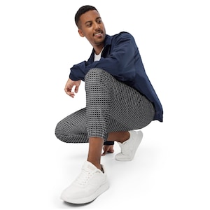 May include: A man wearing a navy blue jacket and black and white patterned pants. He is sitting with his legs crossed and wearing white sneakers.