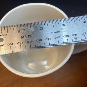 Puede incluir: Una taza de cer&aacute;mica blanca con una regla colocada en la parte superior. La regla est&aacute; marcada en pulgadas y muestra el di&aacute;metro de la taza. La taza mide aproximadamente 7,6 cm de ancho.