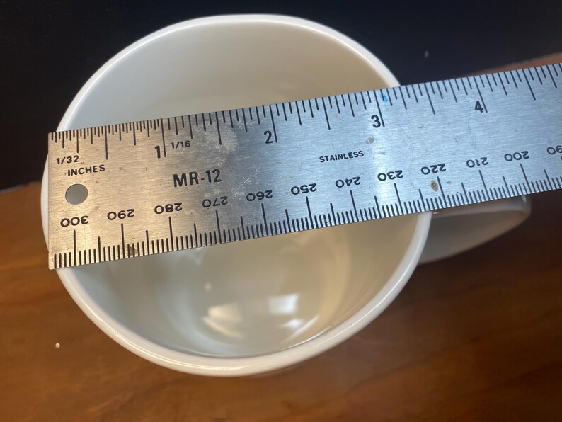 Puede incluir: Una taza de cer&aacute;mica blanca con una regla colocada en la parte superior. La regla est&aacute; marcada en pulgadas y muestra el di&aacute;metro de la taza. La taza mide aproximadamente 7,6 cm de ancho.