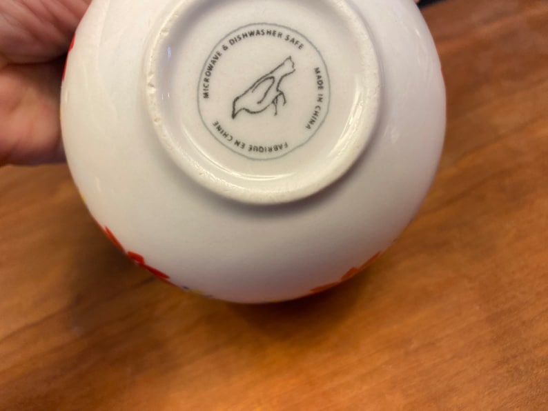 K&ouml;nnte beinhalten: Wei&szlig;er Keramiknapf mit farbenfrohem Blumendesign. Der Boden der Sch&uuml;ssel zeigt eine schwarze Vogelillustration in einem Kreis mit dem Text "MICROWAVE & DISHWASHER SAFE" und "MADE IN CHINA".