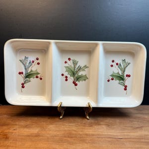 Könnte beinhalten: Ein rechteckiger, cremefarbener Keramik-Servierteller mit drei Fächern. Jedes Fach zeigt ein Stechpalmen- und Beeren-Design in Grün und Rot. Der Teller steht auf einem goldfarbenen Metallständer, ideal für Snacks oder Vorspeisen.