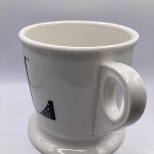 May include: White ceramic mug with a black and white geometric design on the front. The mug has a handle and a wide base.