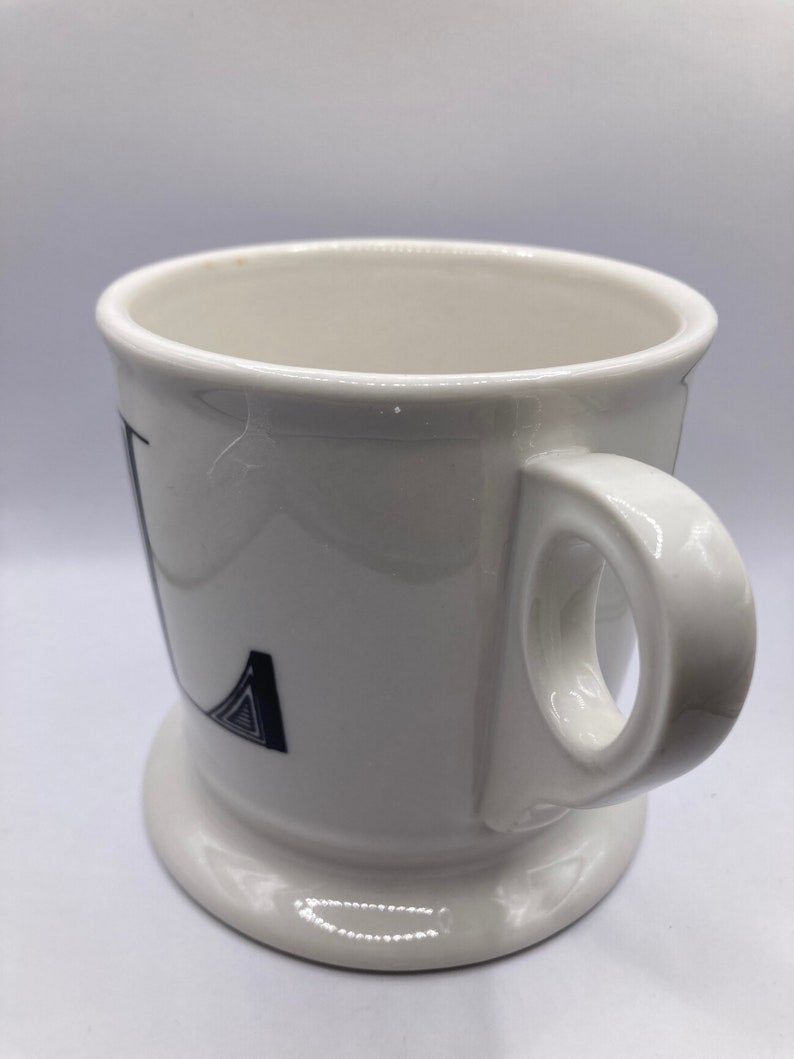 May include: White ceramic mug with a black and white geometric design on the front. The mug has a handle and a wide base.