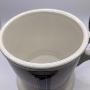 May include: White ceramic shaving mug with a black and grey design. The mug has a wide, round base and a handle.