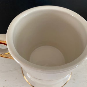 May include: White ceramic shaving mug with a gold rim and handle. The mug has a cylindrical shape and a wide, shallow base.