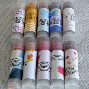 Könnte beinhalten: Zehn Lippenbalsam-Tuben mit bunten Etiketten. Die Etiketten zeigen verschiedene Designs, darunter geometrische Muster, Blumen und Vögel. Der Text auf den Etiketten enthält den Namen "Randalia Bee Hives" und die Worte "Lip Balm Tint".