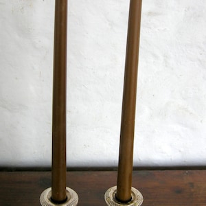 May include: Two brown candles in silver candle holders. The candles are tall and slender, and the holders have a simple, elegant design.