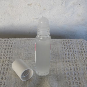 May include: A clear glass roller bottle with a white cap and a white roller ball. The bottle is filled with a clear liquid.