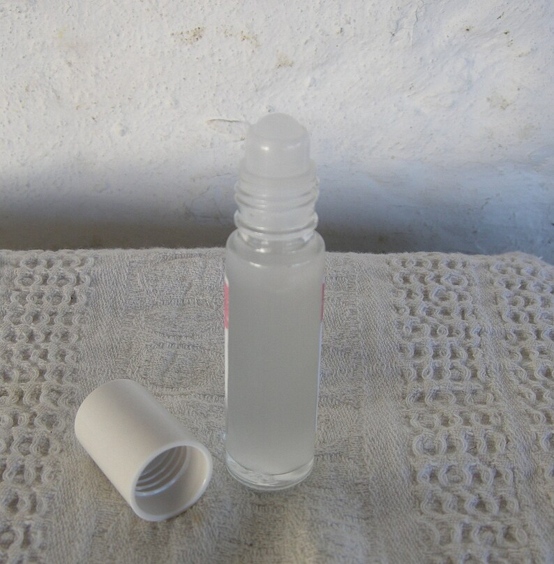 May include: A clear glass roller bottle with a white cap and a white roller ball. The bottle is filled with a clear liquid.