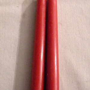 Könnte beinhalten: Zwei rote Kerzen mit weißen Dochten.