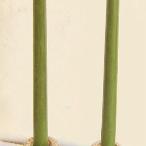 Puede incluir: Dos candelabros de plata con velas verdes. Los candelabros tienen una base cuadrada y una parte superior redonda. Las velas son altas y delgadas.