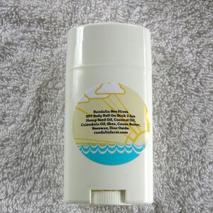 May include: White deodorant stick with a yellow and blue label that reads "Randalia Bee Hives SPF Body Roll On Stick 2.5oz Hemp Seed Oil, Coconut Oil, Calendula Oil, Shea, Cocoa Butter, Beeswax, Zinc Oxide. randaliafarm.com"