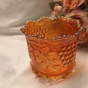May include: A vintage orange glass bowl with a grape design. The bowl has a scalloped edge and a textured surface.