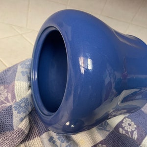 May include: A blue ceramic cookie jar with a rounded, slightly misshapen design. The jar is empty and the lid is off.
