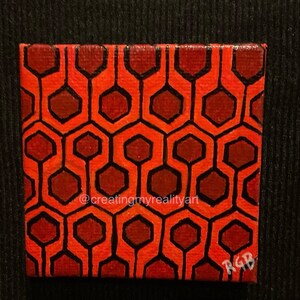 Puede incluir: Una peque&ntilde;a pintura sobre lienzo con un patr&oacute;n geom&eacute;trico rojo y marr&oacute;n. El patr&oacute;n es un dise&ntilde;o repetitivo de hex&aacute;gonos y l&iacute;neas. La pintura est&aacute; firmada "RGB" en la esquina inferior derecha. La pintura est&aacute; sobre un fondo negro.