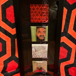 Puede incluir: Un conjunto enmarcado de cuatro peque&ntilde;as pinturas que representan escenas de la pel&iacute;cula "El Resplandor". Las pinturas incluyen el ic&oacute;nico patr&oacute;n de la alfombra roja, un primer plano del personaje de Jack Nicholson, una p&aacute;gina de un libro con salpicaduras de sangre y una escena de pasillo con un ni&ntilde;o peque&ntilde;o con un su&eacute;ter rojo.