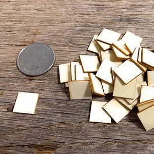 May include: A pile of small, unfinished, square wooden pieces, approximately the size of a US quarter, on a wooden surface.