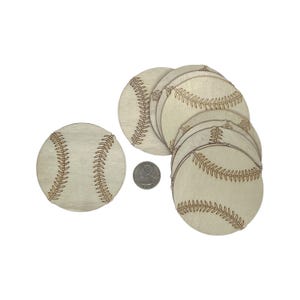 May include: A stack of unfinished wooden baseball-shaped ornaments. The ornaments are approximately 3 inches in diameter and have a natural wood finish.