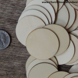 May include: A pile of 2.5 inch unfinished wood circles, arranged in a circular pattern. The circles are a light beige color and have a smooth surface. A US quarter is included for size reference.