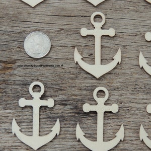 May include: A set of seven unfinished wooden anchor shapes, each approximately the size of a US quarter. The anchors are arranged in a staggered pattern on a wooden surface.