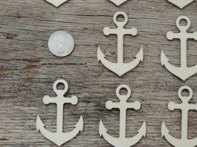 May include: A set of seven unfinished wooden anchor shapes, each approximately the size of a US quarter. The anchors are arranged in a staggered pattern on a wooden surface.