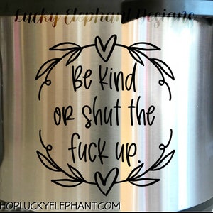 May include: A stainless steel mug with a black vinyl decal that reads "Be kind or shut the fuck up." The decal is surrounded by a wreath of leaves and hearts.