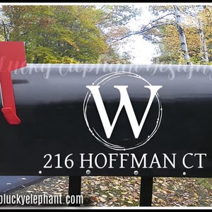 Puede incluir: Buzón negro con una calcomanía de monograma blanco de la letra "W" dentro de un círculo con puntos. La dirección "216 HOFFMAN CT" también está en el buzón.
