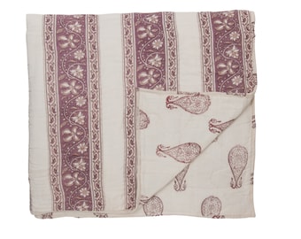 May include: A reversible quilt with a cream background. One side features vertical stripes with floral and paisley patterns in a muted purple. The other side has a paisley design in the same purple color. The quilt is folded, showing both sides.
