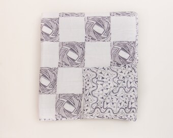 May include: A white fabric with a checkered pattern. Each square features a black and white geometric design. The fabric is folded in half.