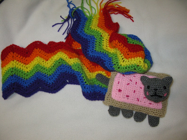 May include: A crocheted rainbow scarf with a crocheted cat-shaped toast with pink frosting and sprinkles.