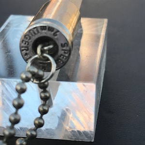 May include: A silver bullet casing necklace with a silver chain. The bullet casing has the text "Win 7mm SPR" engraved on it.