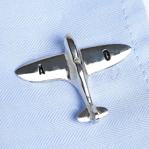 Puede incluir: Gemelos de avión de plata con las letras 'A' y 'O' en las alas.