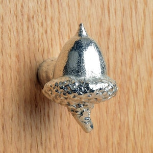 May include: A silver acorn-shaped door knob with a detailed textured design.