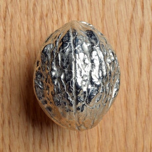 May include: A silver-colored metal walnut, with a detailed, textured surface, resembling the natural ridges of a walnut shell.