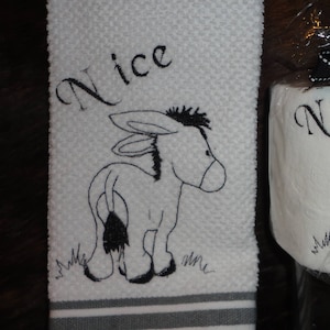 May include: White kitchen towel with gray stripes and a black embroidered donkey with the word "Nice" above it. A white toilet paper roll with a black embroidered donkey and the word "Nice" above it.