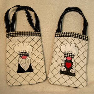 May include: Two small white fabric bags with black and white checkered trim. Each bag has a black and white embroidered gnome with a white chef's hat and a red heart.