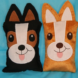 May include: Two plush dog-shaped pillows, one black with brown ears and one brown with white ears. Both pillows have embroidered faces with white noses, black eyes, and pink tongues.