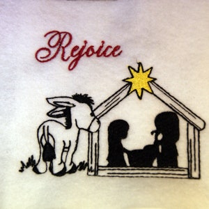 May include: Embroidered white fabric with a black donkey, a manger with two figures inside, and a yellow star above. The text "Rejoice" is embroidered in red.