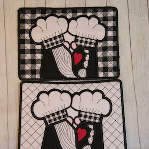 May include: Two black and white quilted fabric squares with a black and white checkered pattern. Each square features a pair of white chef hats with pink accents and a red heart. The chef hats are embroidered with black lines.
