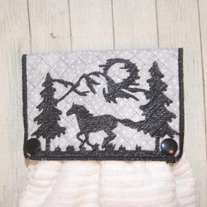 May include: A gray and black quilted kitchen towel holder with a black embroidered design of a horse running through a forest. The holder has two black buttons.