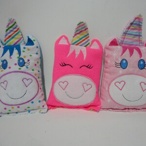 May include: Three plush unicorn pillows with embroidered faces and rainbow horns. The pillows are pink, white with colorful polka dots, and pink with glitter.