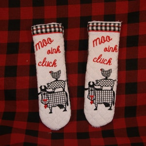 May include: Two white pot holders with black and white embroidered farm animals and the text "moo oink cluck". The pot holders are on a red and black checkered background.