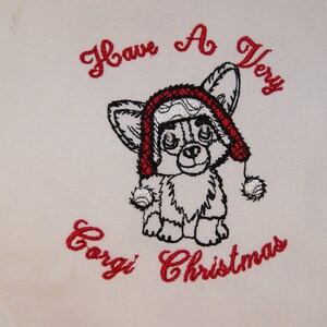 Może przedstawiać: Haftowany wzór przedstawiający corgi w czerwono-białym kapeluszu Świętego Mikołaja z tekstem "Have A Very Corgi Christmas".