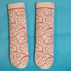 May include: Two white fabric pot holders with red embroidered swirls.